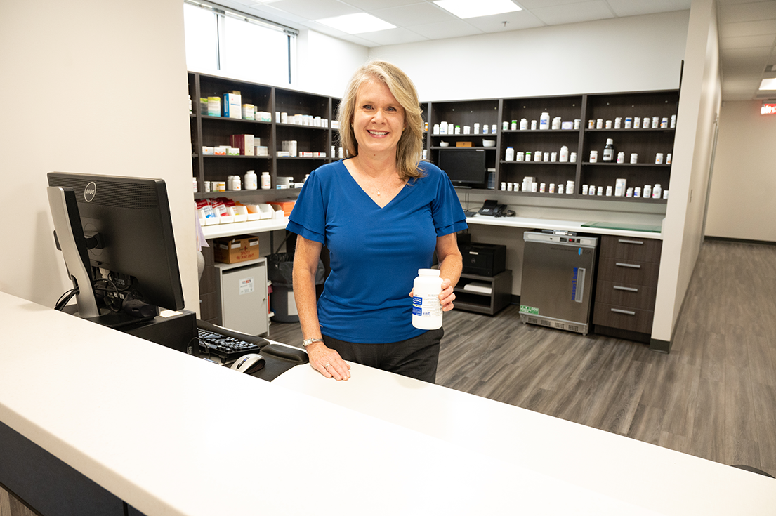 pharmacist Jennifer Daniel smiling behind pharmacy counter holding pill bottle